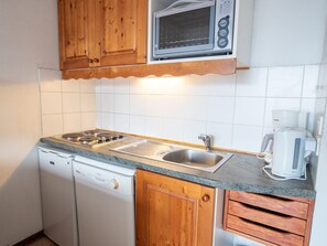 Eine kompakte Küche mit Holzausstattung, einer integrierten Mikrowelle, einem Geschirrspüler und einer Kaffeemaschine.