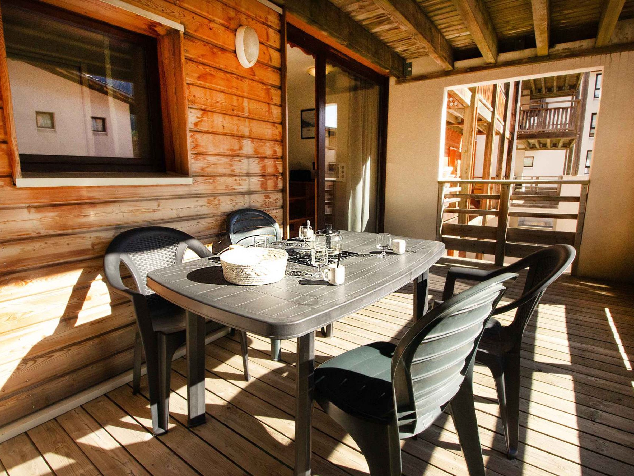 A wooden deck with a table and chairs, a window, and a view of a building.
