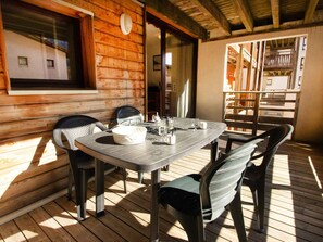 Eine Holzterrasse mit Tisch und Stühlen, einem Fenster und Blick auf ein Gebäude.