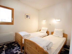 Ein Zimmer mit zwei Holzbetten, einem Heizkörper, einem Fenster und einer Wandleuchte.