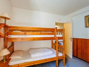 Ein Stockbett mit Holzrahmen, ein Nachttisch mit Lampe und eine Tür zu einem anderen Raum.