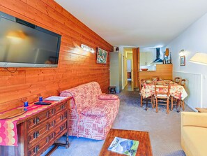 Ein gemütliches Wohnzimmer mit einer Couch, Holzmöbeln, einem Essbereich mit Tisch und Stühlen sowie einem an der Wand befestigten Fernseher.