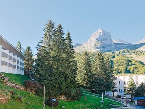 Eine gebirgige Landschaft mit einem markanten Gipfel, umgeben von Grünflächen und Gebäuden.