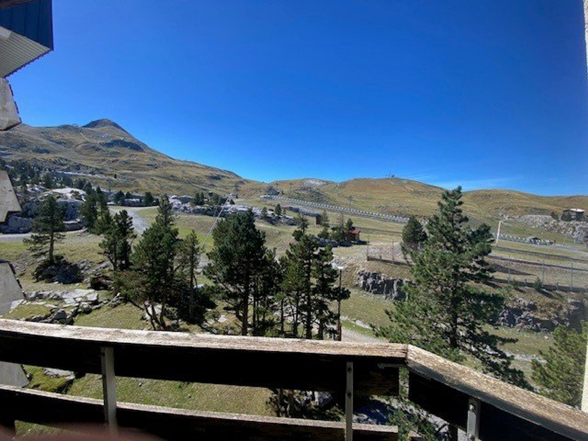 A mountainous landscape with a clear sky, a wooden deck, and a distant view of a town and railway tracks.