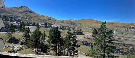 A mountainous landscape with a clear sky, a wooden deck, and a distant view of a town and railway tracks.