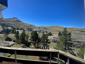 A mountainous landscape with a clear sky, a wooden deck, and a distant view of a town and railway tracks. - Practical apartment, slopes view - 5 guests (Arette)