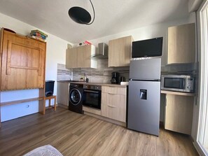 A compact kitchen with wooden cabinets, a built-in washing machine, a refrigerator, and a microwave. - Practical apartment, slopes view - 5 guests (Arette)
