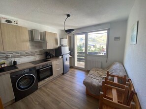 A compact kitchen with a washing machine, a dining area with a table and chairs, and a large window providing a view of the outdoors. - Practical apartment, slopes view - 5 guests (Arette)