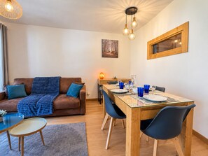 Uma sala de estar acolhedora com um sofá marrom, uma mesa de jantar de vidro e cadeiras azuis, e teto de madeira.