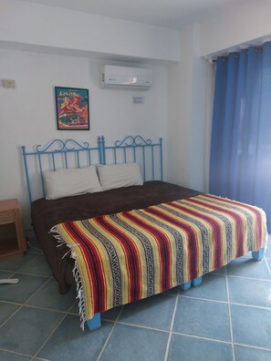 Ein Zimmer mit einem Bett, einer Wandklimaanlage, einem Poster und einem Fenster mit Vorhängen.