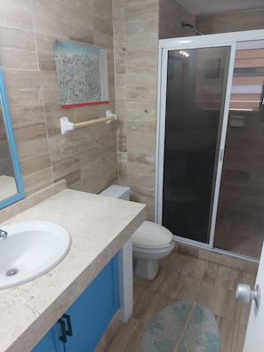 Et badeværelse med vask, toilet og bruseområde.