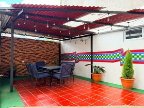 Un patio techado con pared de ladrillo, una mesa con sillas y plantas en macetas.