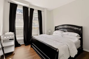 A bedroom with a black headboard, white bedding, a white crib, and a window with black curtains. - Spacious 2BR Near Downtown Indy | Sleeps 6 (Indianapolis)