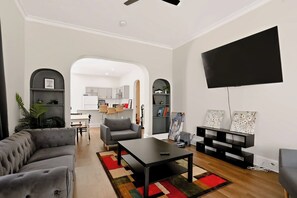Un salón moderno con un sofá gris, una mesa de centro negra y un televisor montado en la pared.