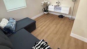 Una sala moderna con un sofá, un televisor de pantalla plana, un mueble blanco pequeño y una lámpara de pie.