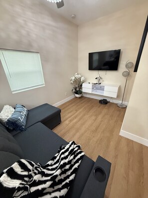 Un salon moderne avec un canapé, un téléviseur à écran plat, un petit meuble blanc et une lampe sur pied.