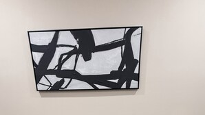 Een kamer met een zwarte tafel en stoelen, een witte vaas met bloemen en een zwart-wit abstract schilderij aan de muur.