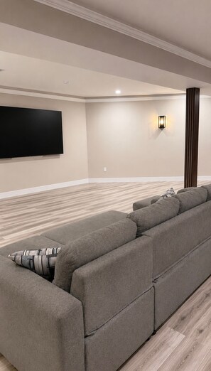 A modern living room with a large sectional sofa, a flat-screen TV mounted on the wall, and a wooden floor. - Entire home in Aldie, Virginia, United States (Aldie)