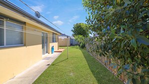 A residential property with a well-maintained lawn, a wooden fence, and a building with a beige exterior. - Salt Gardens – Private Pool & Tea Gardens Retreat (Tea Gardens)