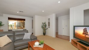 A modern living room with a grey sofa, a coffee table with decorative items, a large potted plant, and a television on a wooden stand. - Salt Gardens – Private Pool & Tea Gardens Retreat (Tea Gardens)