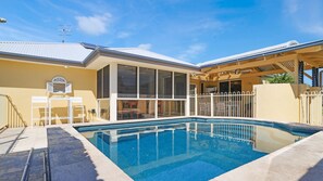 A swimming pool with a clear blue water surface, surrounded by a white fence, and a covered patio area with a yellow roof. - Salt Gardens – Private Pool & Tea Gardens Retreat (Tea Gardens)