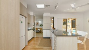 A modern kitchen with a central island, built-in appliances, and a view to a pool area. - Salt Gardens – Private Pool & Tea Gardens Retreat (Tea Gardens)