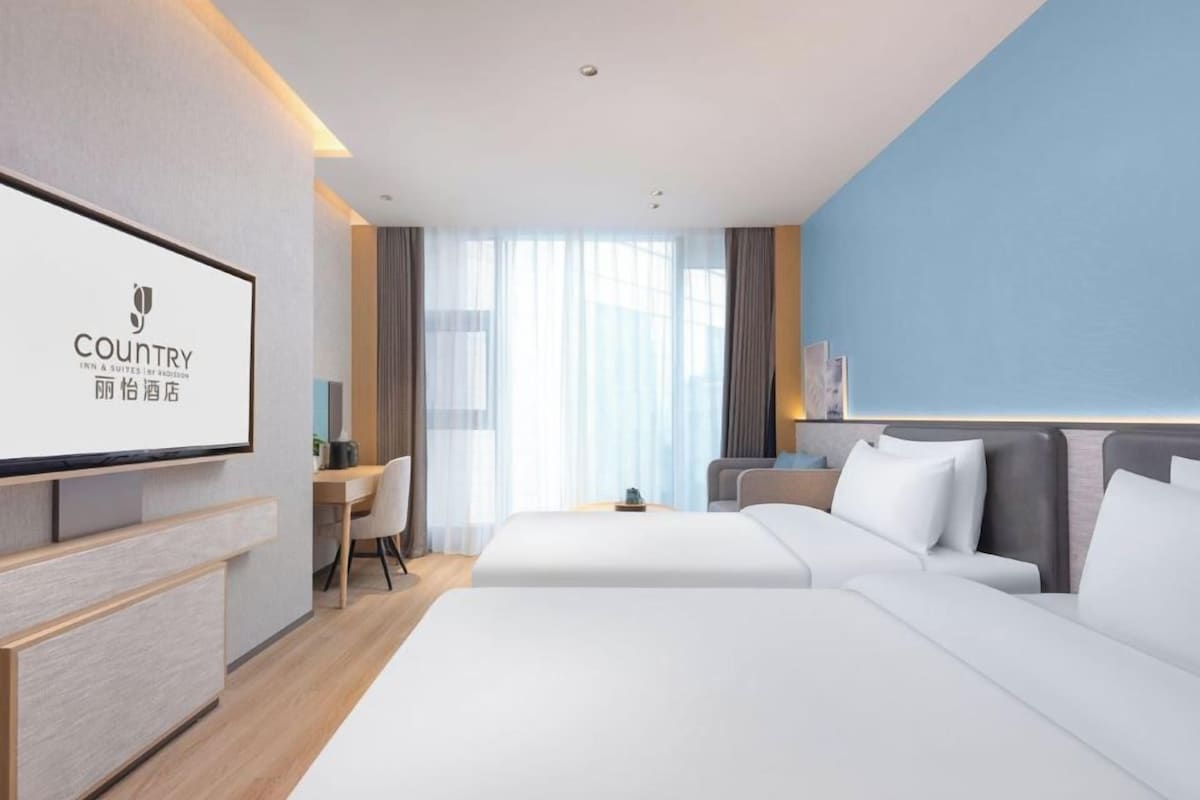 Quarto de hotel com cama, escrivaninha, cadeira e televisão.