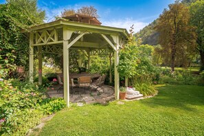Un gazebo con tavolo e sedie, immerso in un giardino ricco di piante e fiori.