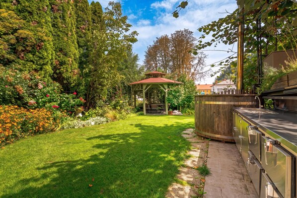 Un giardino con un gazebo, una zona barbecue e una ricca varietà di piante e fiori.