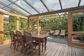 Veranda coperta con tavolo e sedie di legno, immersa nel verde.