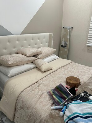 Un lit bien fait, doté d’une tête de lit capitonnée, de plusieurs oreillers et d’une couvre-lit à motifs floraux.