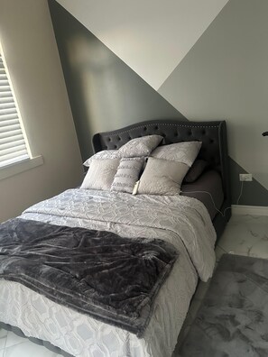 Une chambre à coucher avec un lit, des oreillers, une couverture et une fenêtre avec des stores.