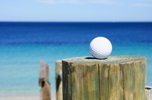 A white golf ball on a wooden post with a clear view of the ocean in the background.