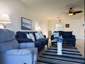 A living room with a sofa, armchair, and a coffee table. There is a ceiling fan and a window with blinds. - 2BR Riverhouse Condo – Pools, Golf & Beaches (Rotonda West)