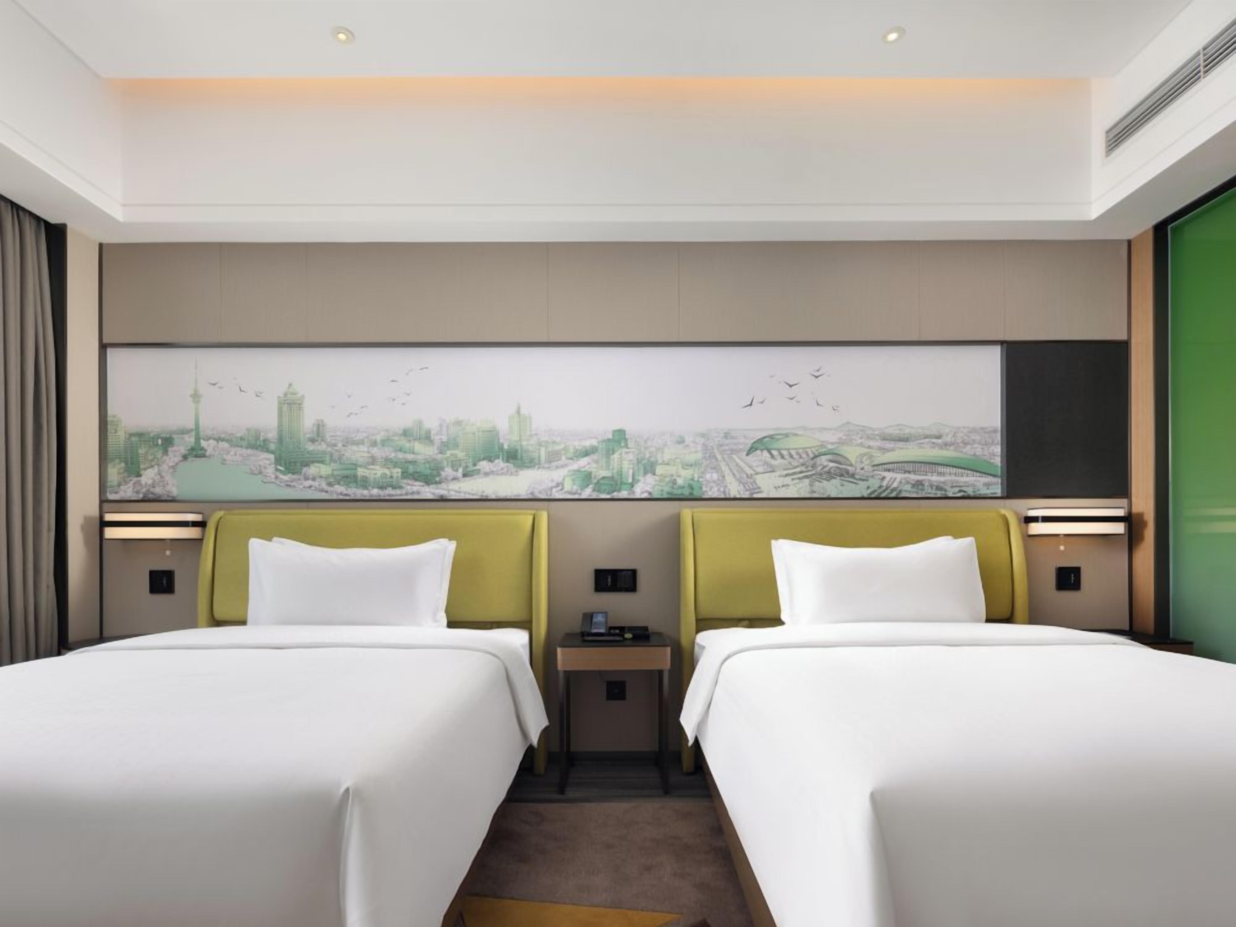Habitación de hotel con dos camas, un mural de paisaje urbano en la pared y vista a la ciudad.