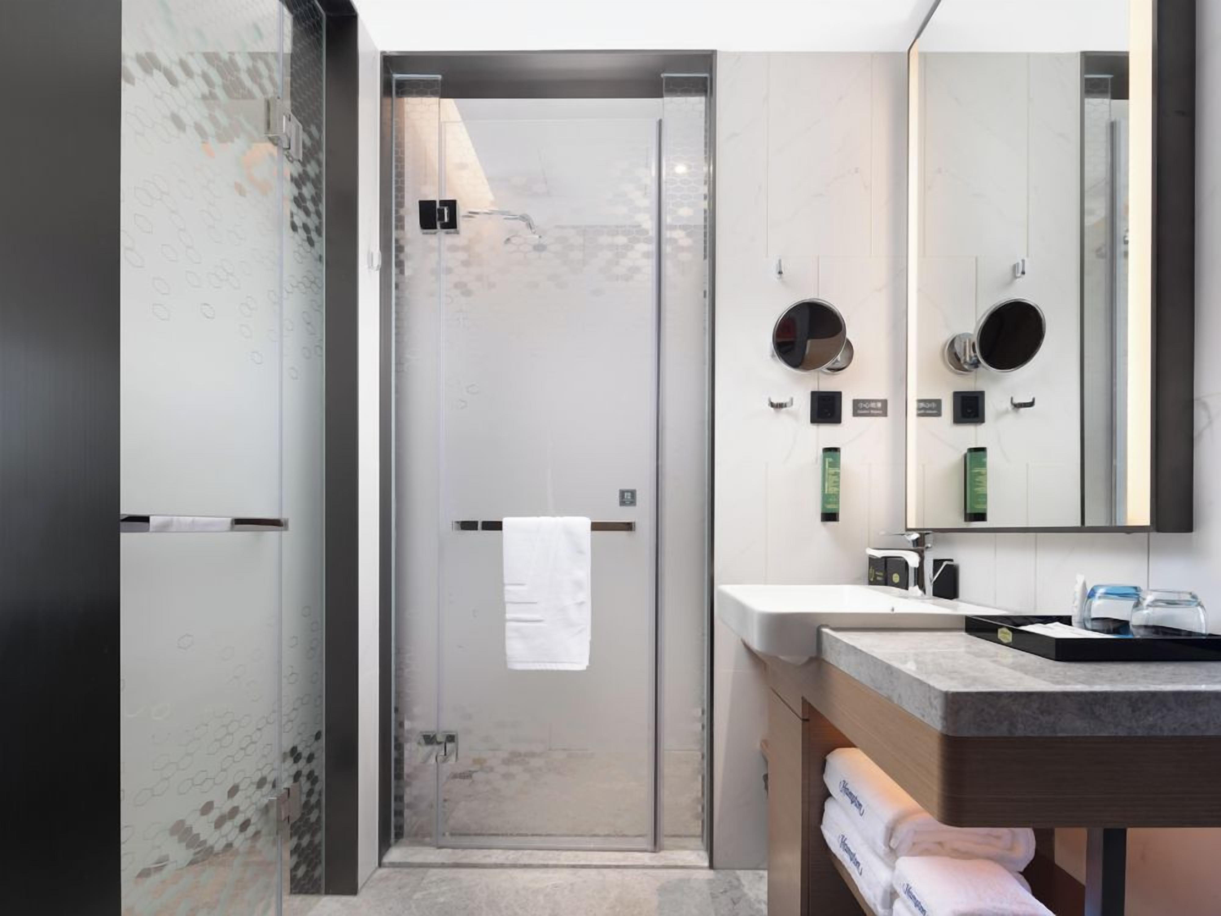 A modern bathroom with a glass shower enclosure, a white sink with a mirror, and a towel rack.