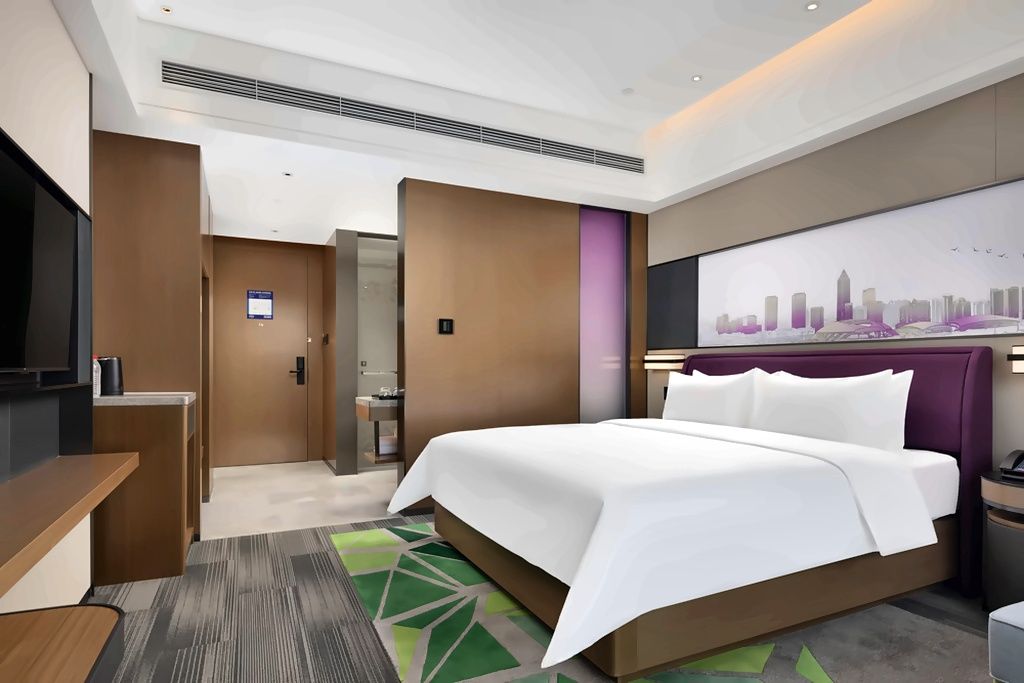 A hotel room with a bed, a desk, a television, and a cityscape painting on the wall.
