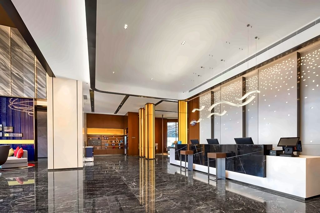 A modern hotel lobby with a reception desk, seating area, and a large wall with decorative lighting.