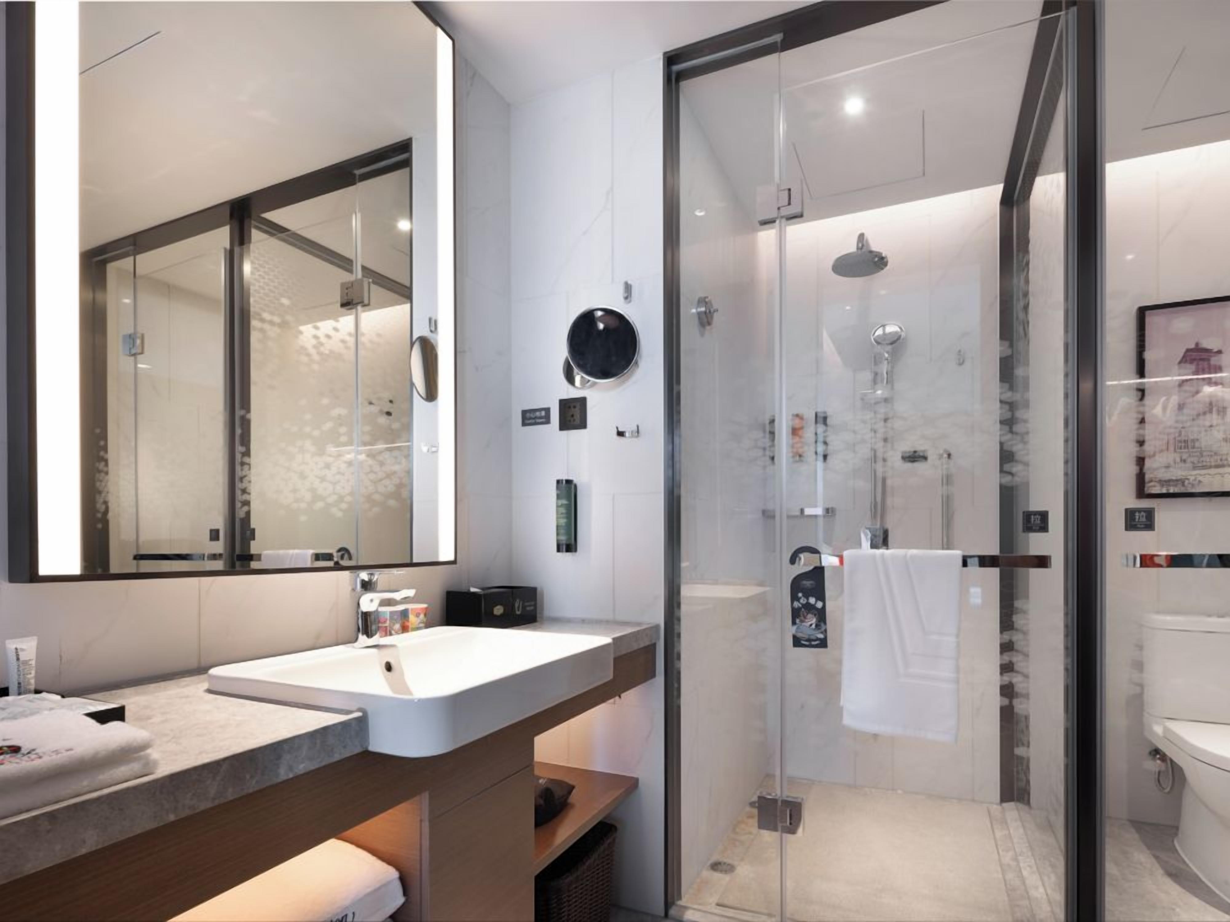 A modern bathroom with a glass-enclosed shower, a large mirror, and a white sink.