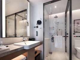 Un baño moderno con ducha envuelta en vidrio, un espejo grande y un lavamanos blanco.