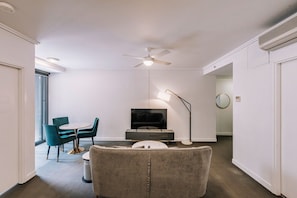Ein modernes Wohnzimmer mit Deckenventilator, Flachbildfernseher, Sofa, Esstisch mit Stühlen und Stehlampe.