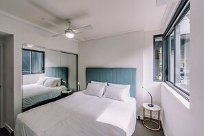Ein Hotelzimmer mit einem großen Bett, einem Deckenventilator, einem Nachttisch, einer Lampe und einem Fenster mit Blick.