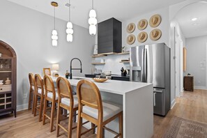 A modern kitchen with a central island, wooden chairs, a stainless steel refrigerator, and decorative hats on the wall. - Stunning Home on Music Row - Rooftop TV, Sauna, & Grill Near Broadway! (Nashville)
