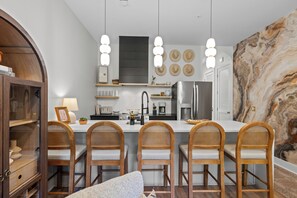 A modern kitchen with a central island, bar stools, and a marble backsplash. - Stunning Home on Music Row - Rooftop TV, Sauna, & Grill Near Broadway! (Nashville)