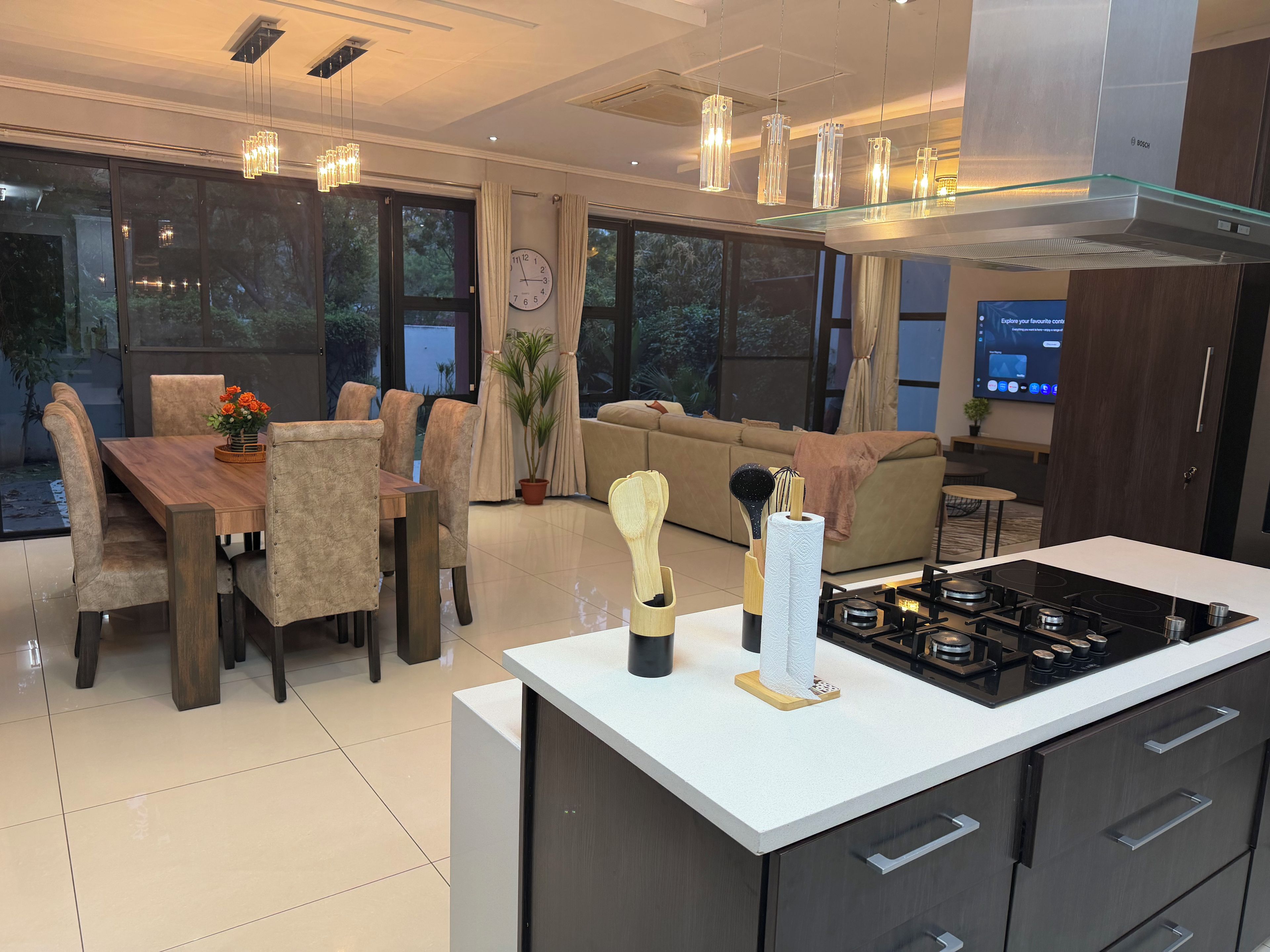 A modern kitchen with a central island, a dining area with a wooden table and chairs, and a living area with a sofa and a TV.