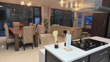 A modern kitchen with a central island, a dining area with a wooden table and chairs, and a living area with a sofa and a TV.