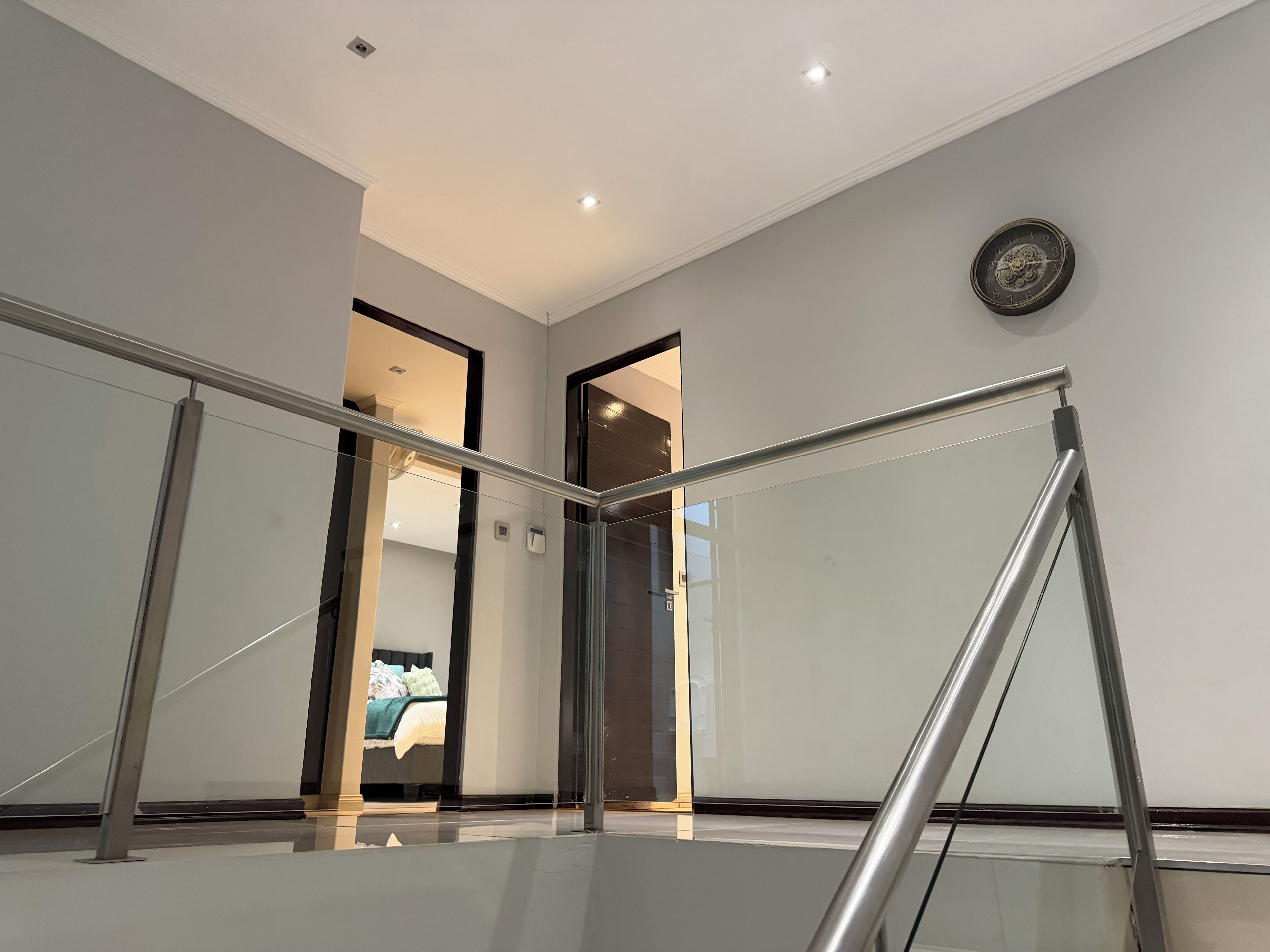 L'intérieur moderne d'un hôtel, avec une rambarde en verre, une horloge au mur et un lit visible à travers une porte ouverte.