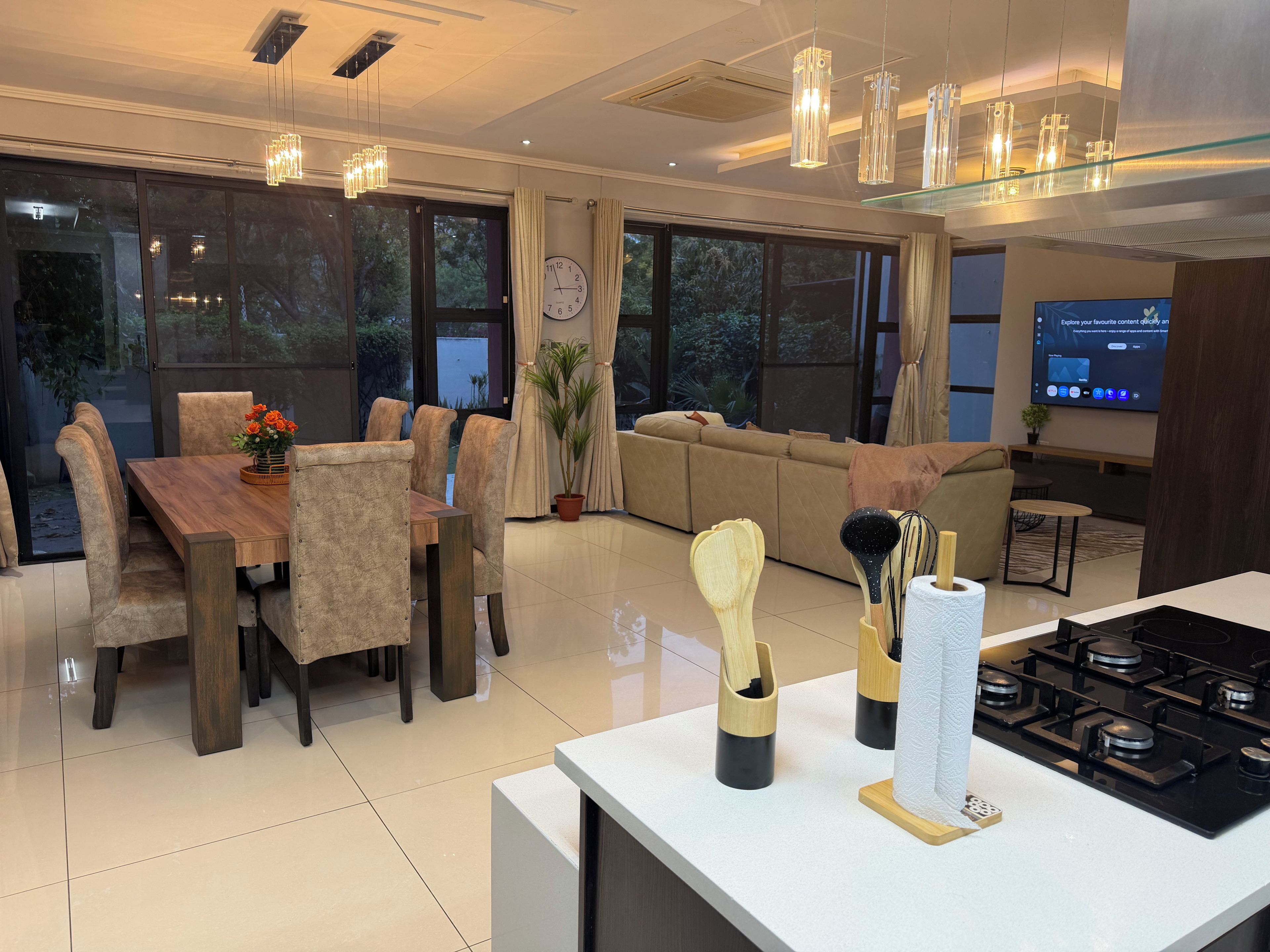 A modern kitchen with a dining area, large windows, and a flat-screen TV.