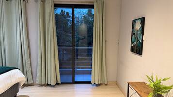 Una camera da letto moderna con un letto, una porta scorrevole in vetro verso un balcone, un quadro al muro e un tavolino con una pianta.
