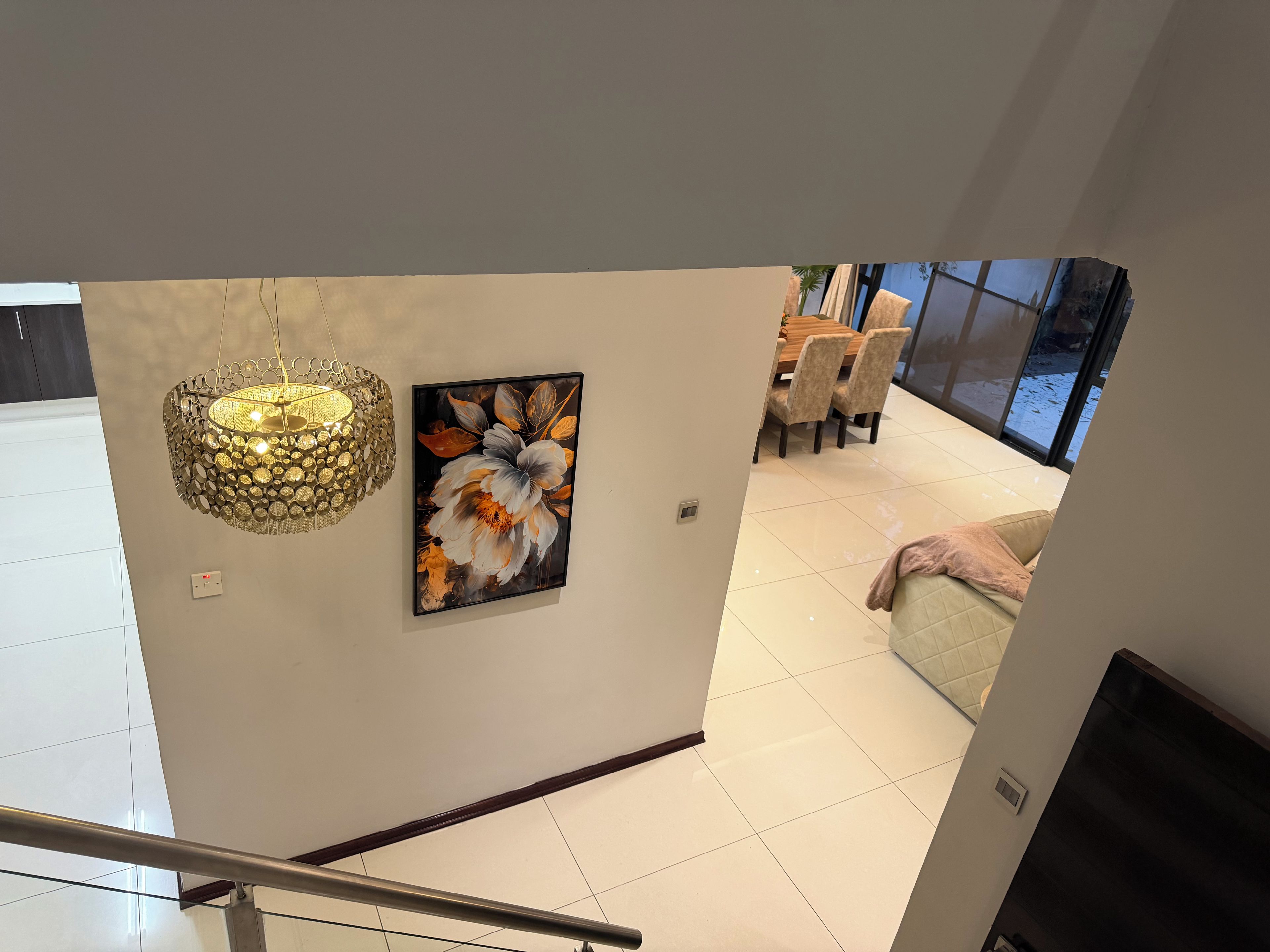 Um interior moderno com uma escada, uma área de refeições com cadeiras e uma obra de arte suspensa na parede.